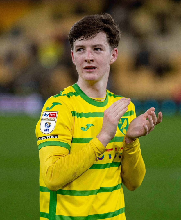 Ein junger Mann in einem gelb-grünen T-Shirt feiert auf einem Fußballfeld, indem er seine Hände klatscht, der Hintergrund ist unscharf.