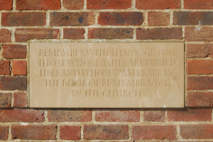 Eine Ziegelwand mit einer Tafel, auf der steht: "Erinnere dich mit Dankbarkeit an diejenigen, deren Asche hier begraben ist und deren Namen im Buch der Erinnerung in der Kirche stehen."