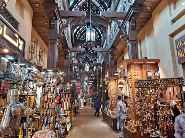 Ein belebter Dubai-Basar mit Menschen, die zwischen Regalen voller Gegenstände hindurchgehen, Wänden mit Texttafeln und einer Decke mit warmem Licht.