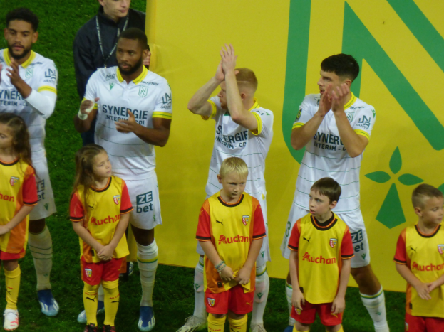 Eine Gruppe von Fußballspielern in Uniformen, die auf einem Feld klatschen, mit einem "Ligue 1"-Schild im Hintergrund.