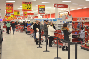 Ein volles Walmart-Geschäft mit Einkaufstüten tragenden Kunden und Einkaufswagen, umgeben von Warenregalen, Schildern und Deckenleuchten.