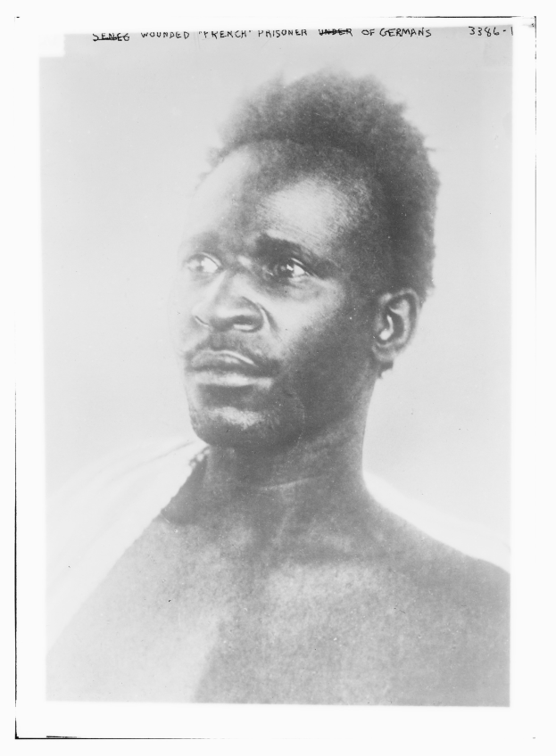 Ein Schwarz-Weiß-Foto eines Mannes mit ernstem Gesichtsausdruck, mit Text oben, der "Seneg Verletzter französischer Gefangener unter Deutschen" lautet.