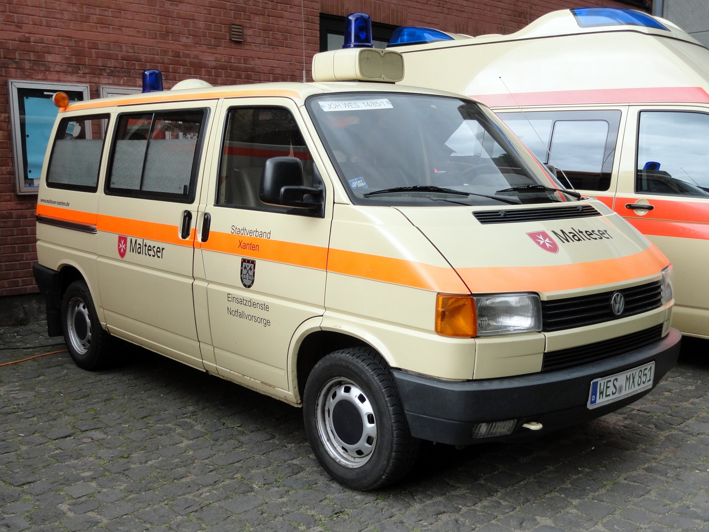 Zwei Rettungswagen nebeneinander vor einem Backsteingebäude mit Fenstern und einer Tür geparkt.