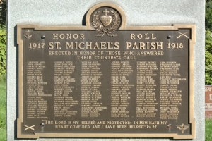Gedenktafel an einer Steinwand in der St. Michael's Parish umgeben von grünem Gras und Bäumen.
