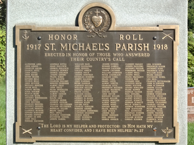 Gedenktafel an einer Steinwand in der St. Michael's Parish umgeben von grünem Gras und Bäumen.
