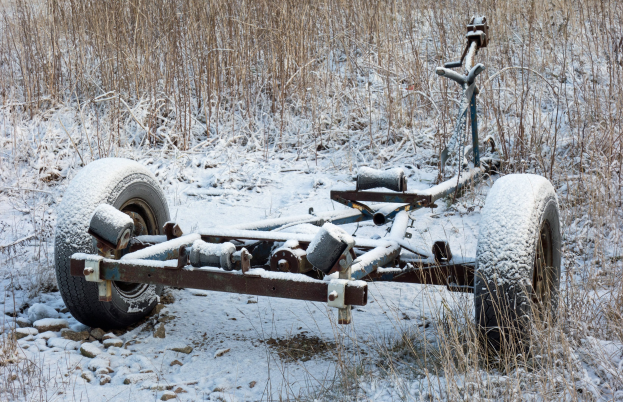 Alter rostiger Anhänger mit Schnee bedeckt in einem verschneiten Feld mit Gras und Steinen.