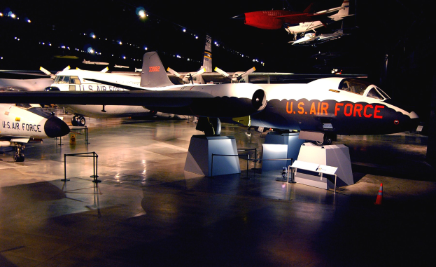 Eine Gruppe von Kampfflugzeugen in einem Museum mit St├Ąnden, Verkehrskegeln und anderen Gegenst├Ąnden auf dem Boden, unter dunkler Hintergrundbeleuchtung.