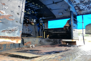 Das Innere eines verrosteten, baufälligen Lastwagens mit sichtbaren Spuren von Abnutzung, vor einem Hintergrund aus Bäumen und einem klaren blauen Himmel.
