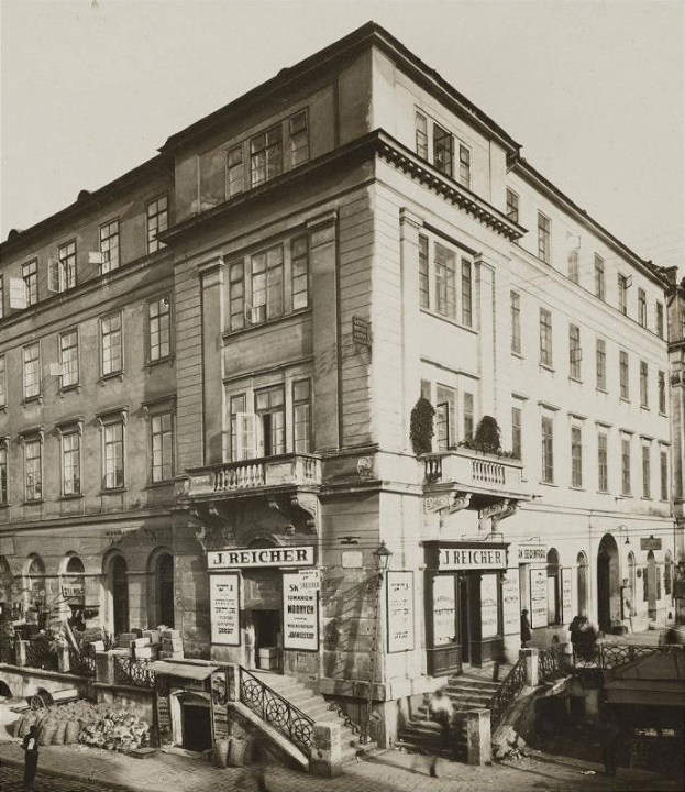 Das J Reicher Hotel in Berlin, ein altes Gebäude mit mehreren Fenstern, Treppen mit Geländern und Töpfen mit Pflanzen, mit ein paar Menschen und einem sichtbaren Himmel im Hintergrund.