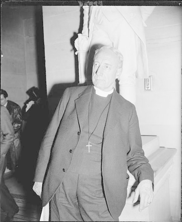 Schwarz-weißes Bild eines Mannes in Anzug und Krawatte neben einer Statue mit einigen Menschen und einer Wand im Hintergrund, das angeblich Papst Johannes Paul II. bei seiner Ankunft im Vatikan zeigt.