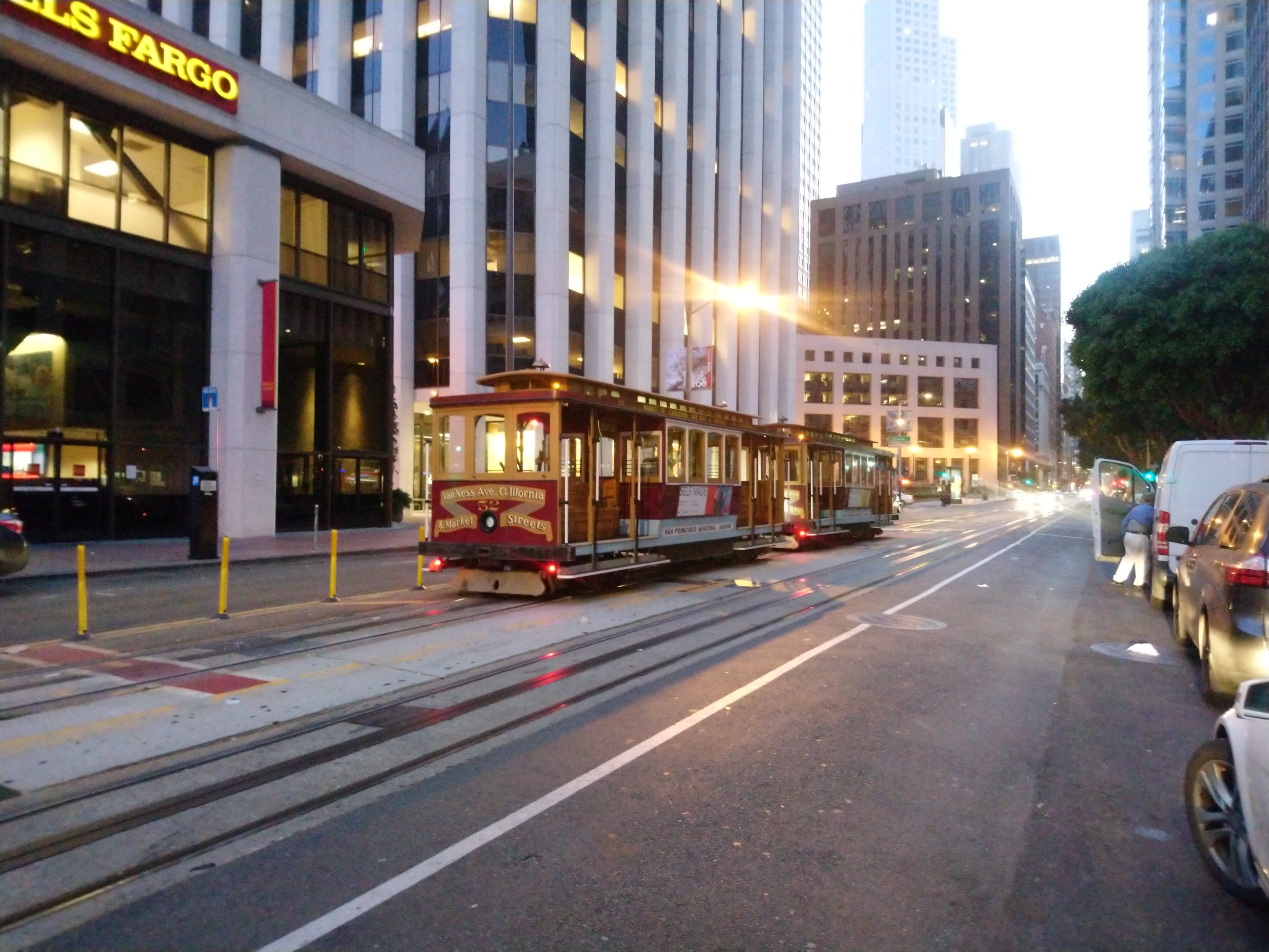 Eine Seilbahn fährt eine Straße in San Francisco mit Fahrzeugen, einem Fußgänger und einem geparkten Van hinunter.