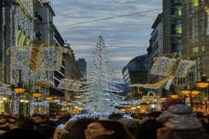 Eine belebte Stadtstraße bei Nacht, geschmückt mit festlichen Weihnachtslichtern, voller Fußgänger und mit einem großen Weihnachtsbaum in der Mitte der Straße.