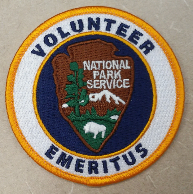 Rundes Patch mit "Volunteer National Park Service Emeritus" in fetter schwarzer Schrift auf einem weißen Hintergrund, umgeben von einem gelben Kreis und einem blauen Rand.