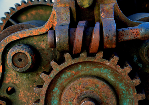 Nahaufnahme eines verrosteten Metallzahnrades mit mehreren Zähnen und Rädern, das Spuren von Alter und Abnutzung zeigt.
