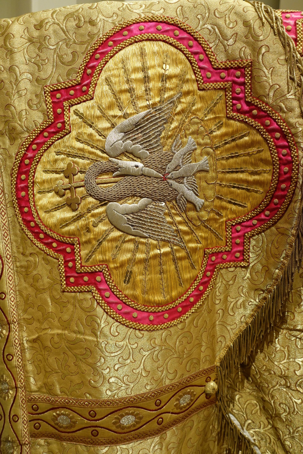 Nahaufnahme eines Priestergewandes mit goldenen und roten Stickereien und detaillierten Mustern, das an einer Wand im Hintergrund zu sehen ist.