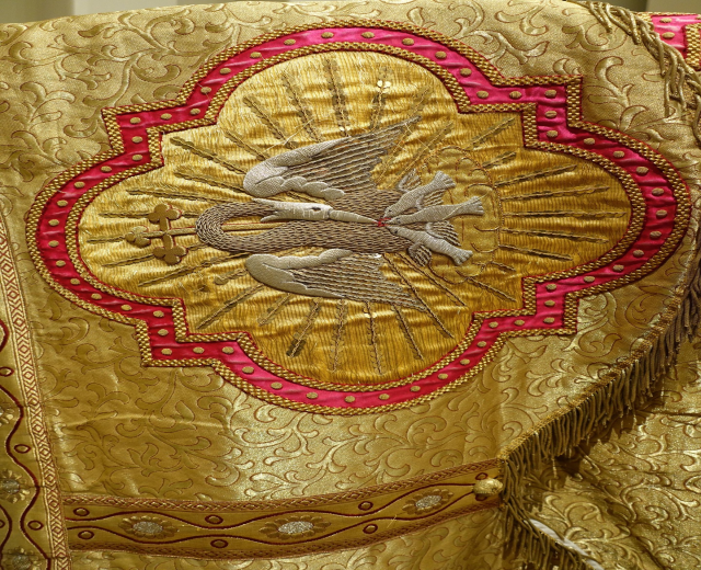Nahaufnahme eines Priestergewandes mit goldenen und roten Stickereien und detaillierten Mustern, das an einer Wand im Hintergrund zu sehen ist.