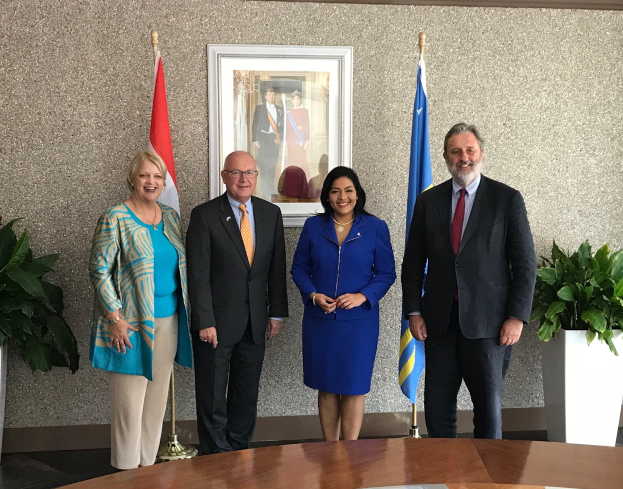 Eine Gruppe strahlender Menschen, die um einen Tisch mit Papieren stehen, umgeben von Fahnen, Topfpflanzen und einem Foto auf dem Wand, feiern die Unterzeichnung eines Memorandums zwischen den Vereinigten Staaten und Kanada.