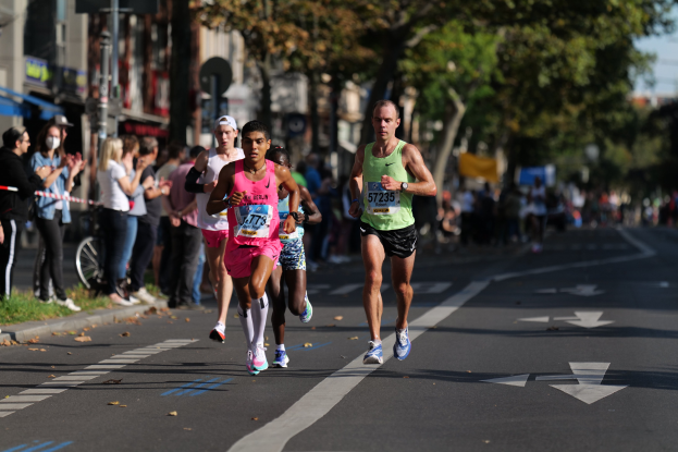 Gruppe von Läufern bei einem Marathon auf einer städtischen Straße mit Zuschauern und urbanen Elementen im Hintergrund.