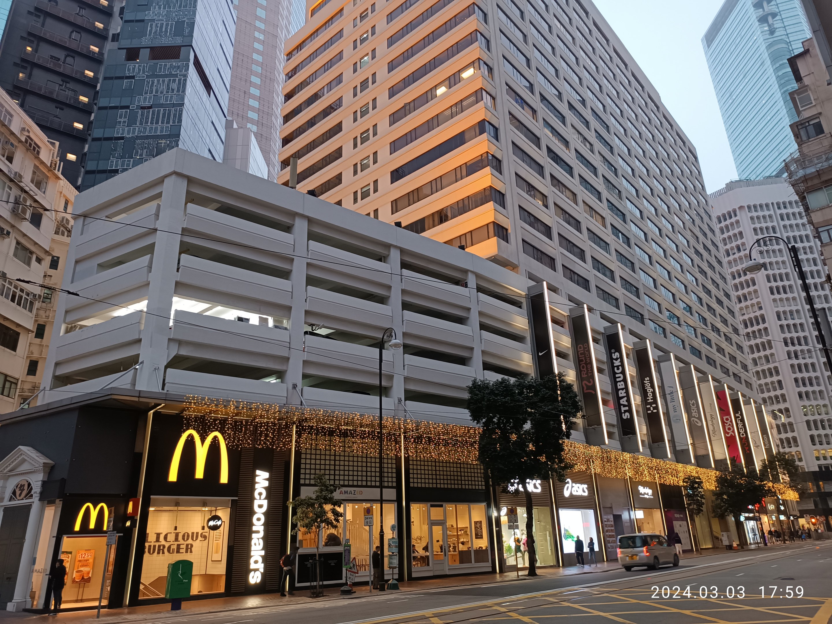 McDonald's-Restaurant auf einer belebten Stadtstraße mit hohen Gebäuden, Fahrzeugen, Fußgängern, Straßenmöblierung, Bäumen und einem klaren Himmel.