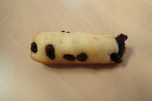 Ein Close-up eines goldbraunen Kekses mit einer leichten Zuckerguss- und Rosinenbestäubung auf einem Holztisch.