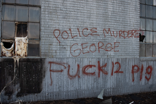 Ein Gebäude mit der Aufschrift "Polizei Mord George Fuck 12 P19" an der Seite, mit Fenstern und diversen Gegenständen davor.