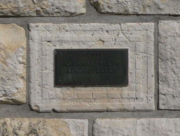 Steinwand mit einem rechteckigen Schild, auf dem "National Youth Administration" in weißer, fetter Schrift auf schwarzem Hintergrund steht.