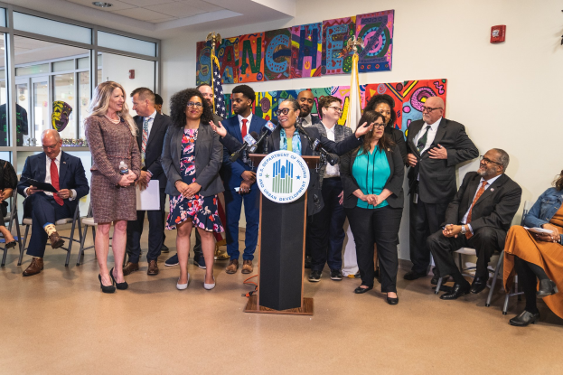 Gruppe von Menschen vor einem Rednerpult mit Mikrofon und einer Tafel mit der Aufschrift "Sancho-Stadtrat tritt dem Stadtrat bei" bei einer Stadtratssitzung.
