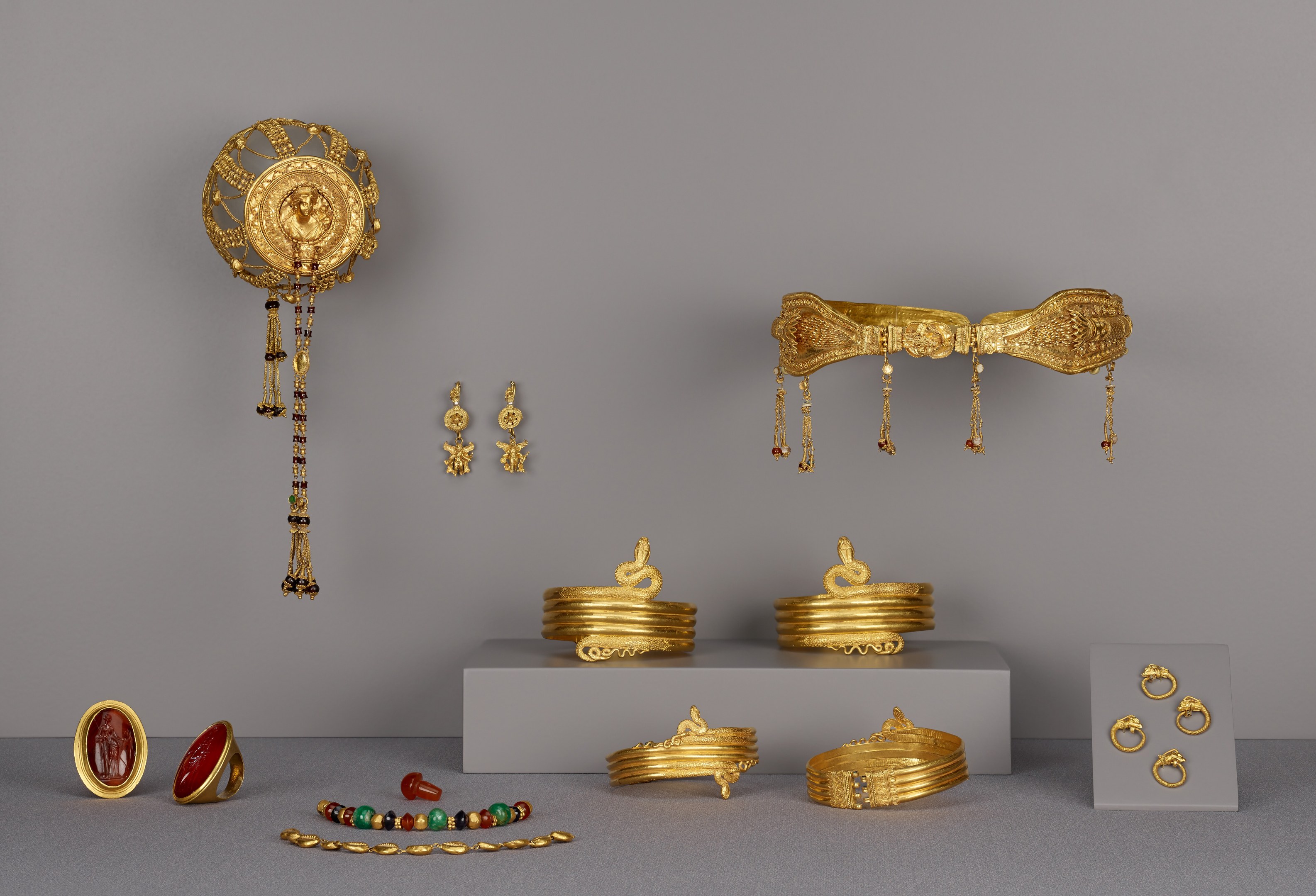 Goldschmuck-Display mit Armbändern, Ringen und weiteren Stücken auf einer Oberfläche, mit zusätzlichen Teilen an der Wand im Hintergrund.