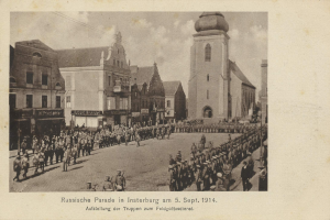 Ein Schwarz-Weiß-Foto eines Umzugs in Insterburg am 5. September 1914 mit vielen Menschen, Gebäuden und bewölktem Himmel sowie Text unten.