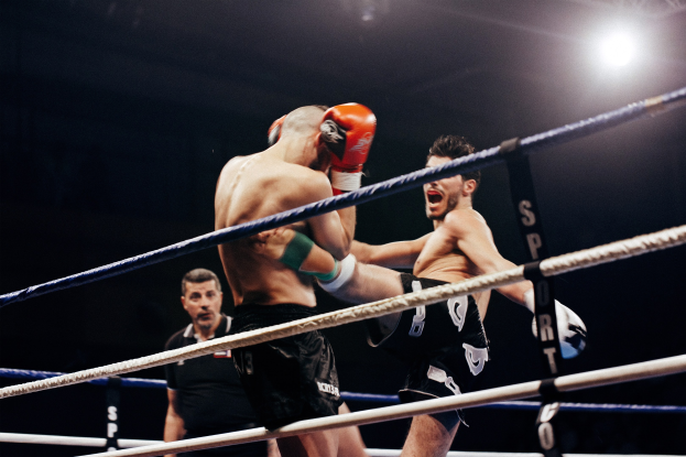 Zwei Boxer im Ring mit einem Schiedsrichter unter hellen Deckenlampen.