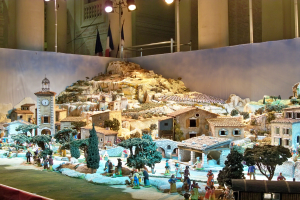 Ausstellung im Museum mit einer detaillierten Darstellung einer Krippe mit Figuren, Strukturen und beleuchteten Elementen vor einem dekorierten Hintergrund.