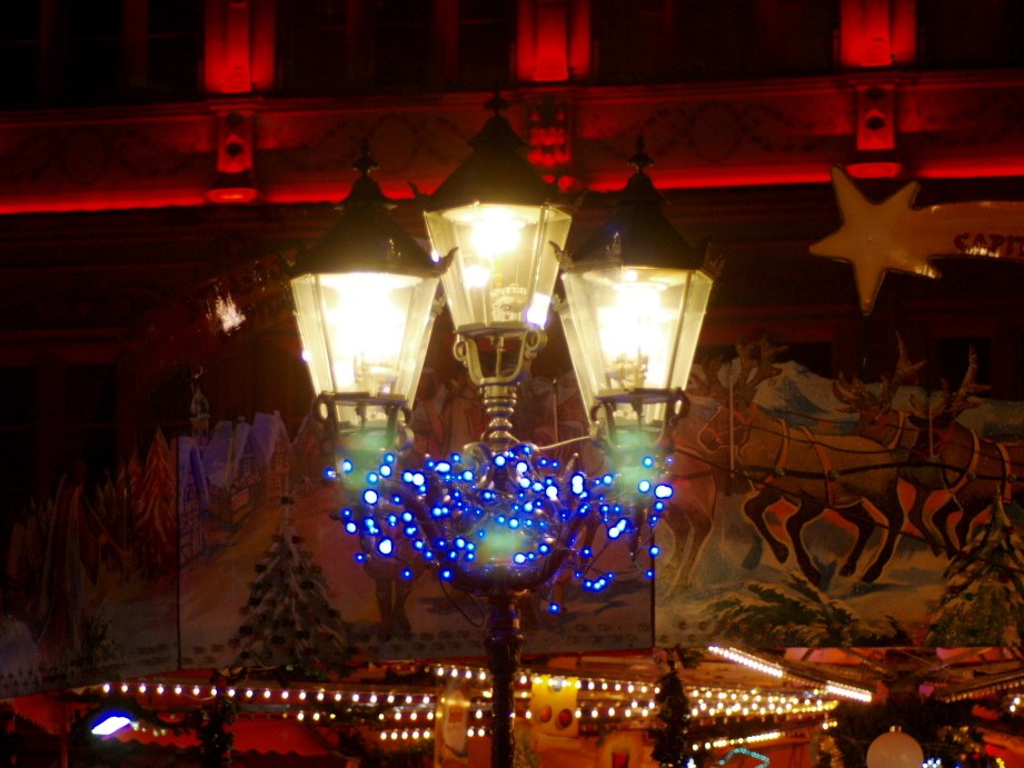 Eine dekorative Straßenlaterne mit Lichtern und Schmuck steht in einer Stadt in der Nacht, mit einem Gebäude im Hintergrund.