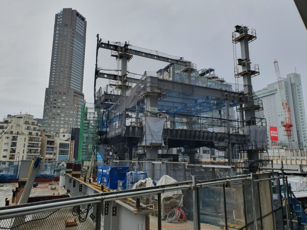Großbaustelle für ein neues Kraftwerk in einer städtischen Gegend, umgeben von einem Metallzaun, mit Gebäuden, Polen, einer Fahne, Fahrzeugen, Drähten und einem bewölkten Himmel.