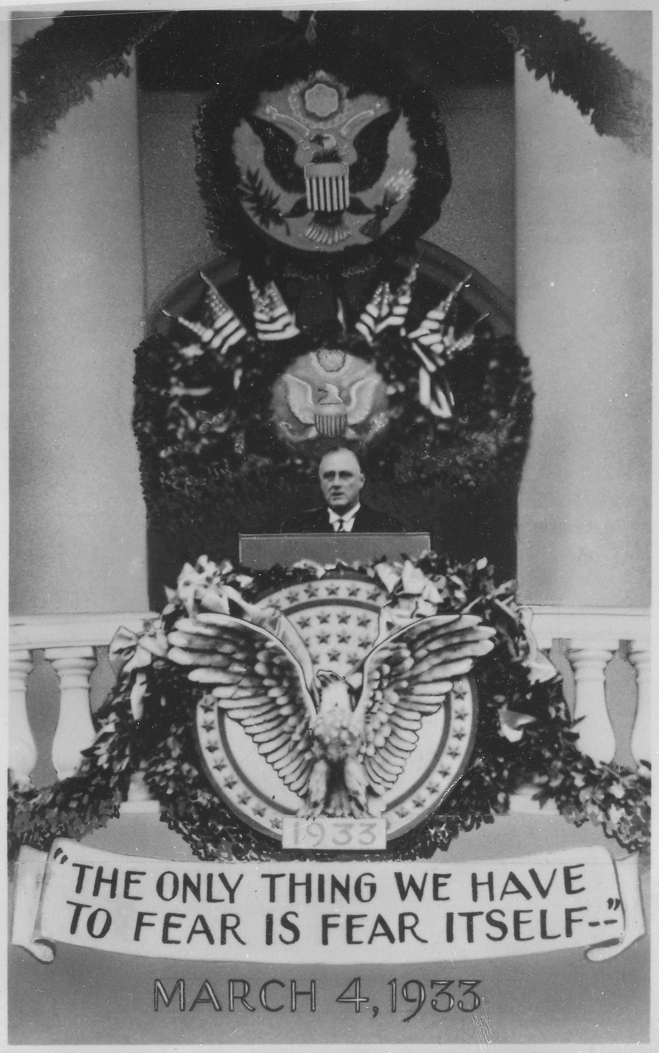 Schwarzes und weißes Foto eines Mannes, der an einem Rednerpult spricht, mit einem Kranz und einem Emblem an der Wand dahinter und dem Zitat "Das einzige, wovor wir uns fürchten müssen, ist die Furcht selbst" unten.