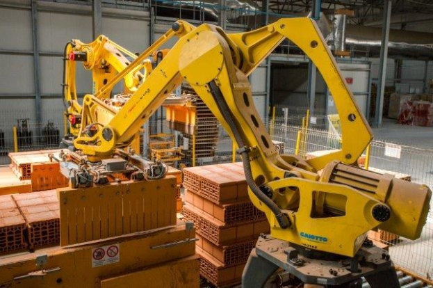 Großes industrielles Lagerhaus mit gestapelten Kisten, Überkopfkranen, Zaun, Versorgungsmasten und einer fernen Wand in einer Fertigungsanlage.