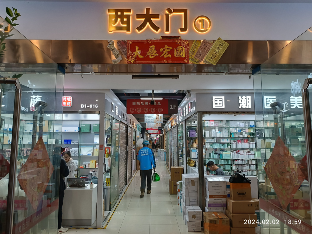 Innenseite einer chinesischen Apotheke mit Glaswänden, Regalen mit Waren, verstreuten Kartons, einer Pflanze auf der linken Seite und einem Namensschild oben.