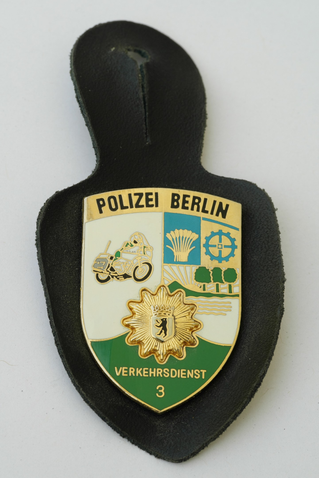 Ein schildförmiges Polizeibadge mit "Polizei Berlin" in schwarzer Fettschrift auf einem blauen Hintergrund mit einem weißen Stern und Rahmen, das auf einer Oberfläche ruht.