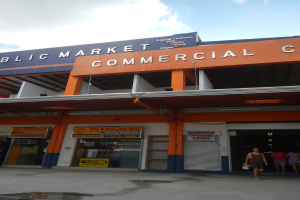 Ein öffentlicher Markt mit Menschen davor, Text auf dem Gebäude und einem sichtbaren Himmel oben.