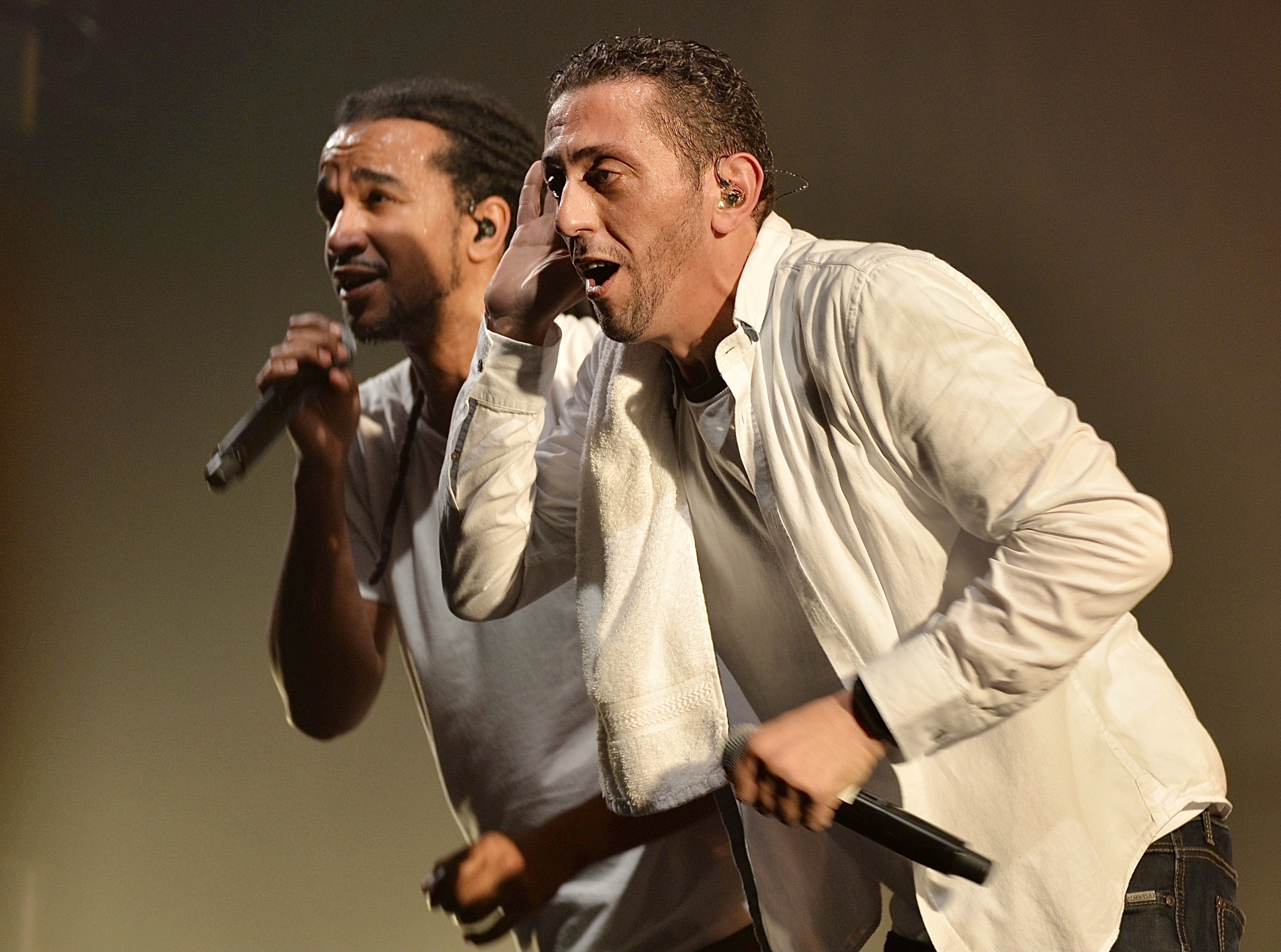 Zwei Männer in legerer Kleidung stehen nebeneinander auf einer Bühne, jeder hält ein Mikrofon während einer Vorstellung.