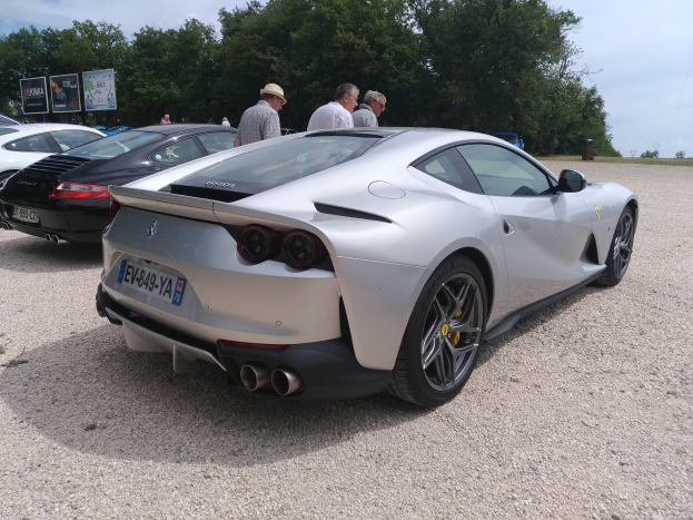 Roter Ferrari 812 Superfast auf dem Goodwood Festival of Speed, umgeben von Menschen mit Mützen, Bäumen, Texttafeln und bewölktem Himmel im Hintergrund.