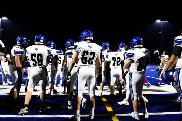 Eine Gruppe von Fußballspielern in Helmen und Stiefeln auf einem Feld unter Flutlicht, bereit zum Spielstart.