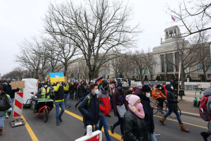 Eine große Gruppe von Menschen marschiert bei einer Demonstration durch eine Straße in Washington, D.C., einige halten Schilder und andere fahren Fahrräder, mit Bäumen und einem Gebäude im Hintergrund bei klarem blauem Himmel am 21. Januar 2020.